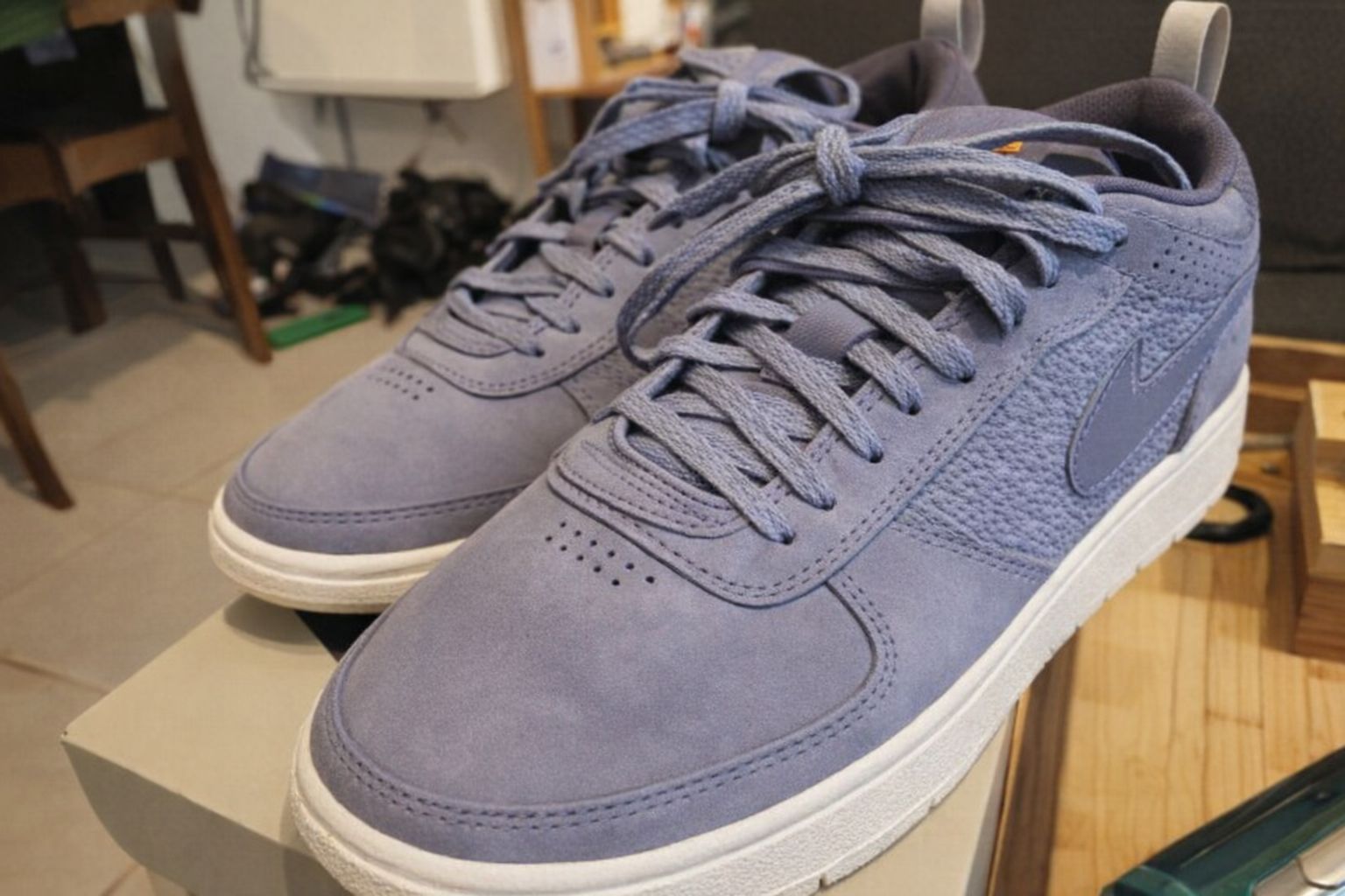 Ett par gråblå sneakers i mocka på en skokartong i en hemmiljö.