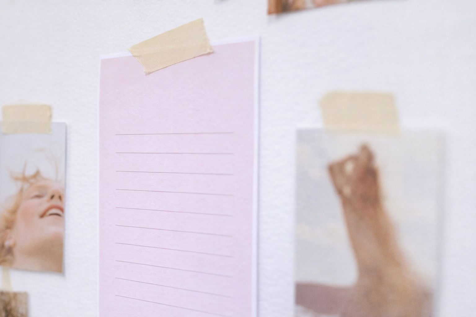En rosa linjerad anteckningssida och fotografier upptejpade på en vit vägg.